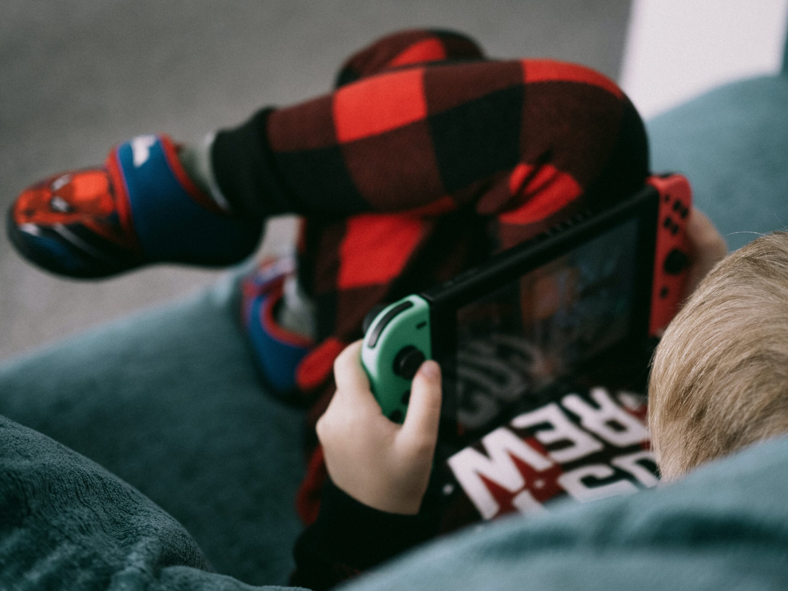 Picture of a boy, in his pajamas, laying on the couch, playing with his Nintendo Switch.